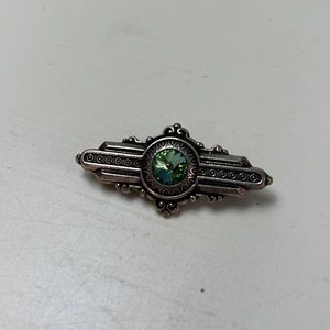 P9. Metallic pin with green glass stone in the middle.